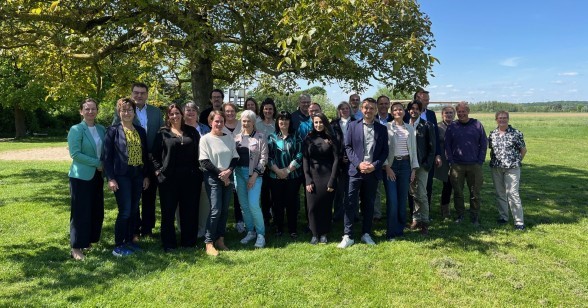 Eine Gruppe von rund 20 Personen steht bei sonnigem Wetter auf einer Wiese unter einem großen Baum und blickt in die Kamera.