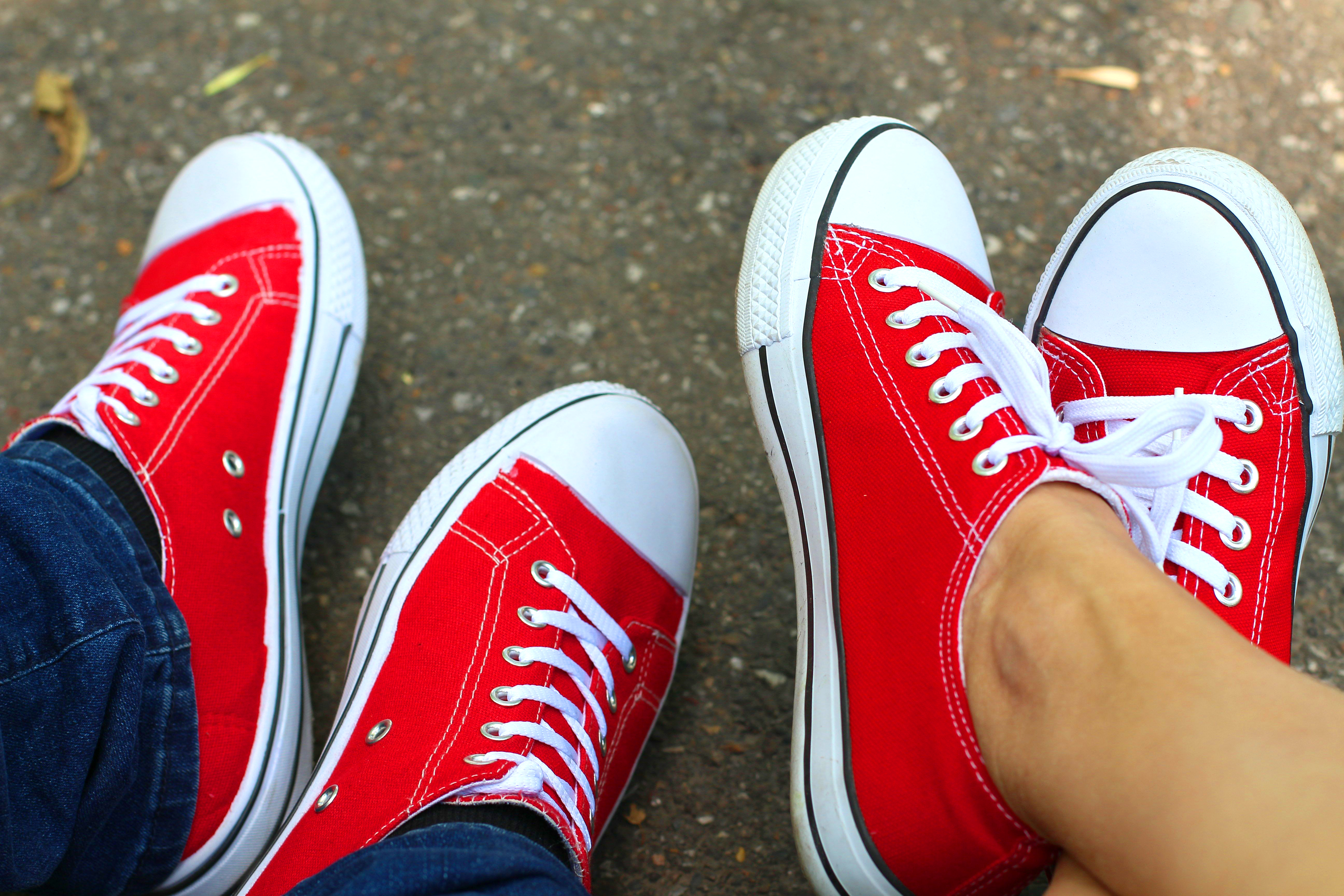 Zwei Personen tragen rote Schuhe mit weißer Sohle und weißen Schnürsenkeln. Eine Person trägt eine braue Hose, die andere Person hat nackte Beine.