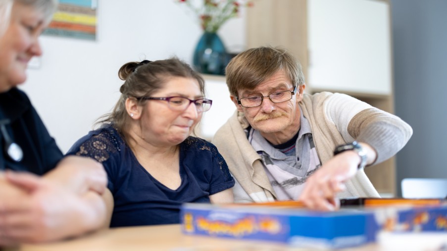 Zwei Kund*innen die gemeinsam mit einer Mitarbeiterin ein Spiel spielen.