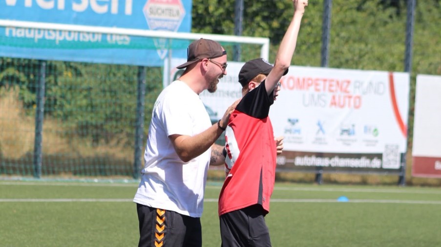 Ein Mann mit einem weißen Trikot und ein Mann mit einem roten Trikot, der den Arm hebt, stehen nah aneinander.