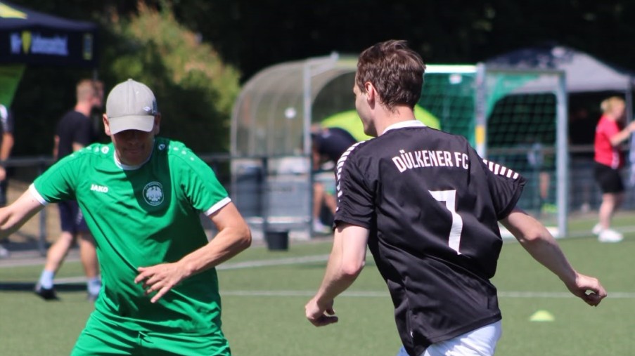 Zwei Fußballspieler in Grün und Schwarz-Weiß konzentrieren sich auf den Ball; einer trägt die Nummer 7.
