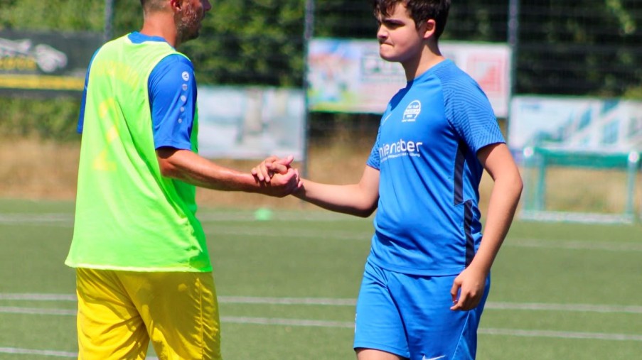 Zwei Fußballspieler geben sich die Hand: einer in Blau, der andere in Gelb mit grünem Leibchen.
