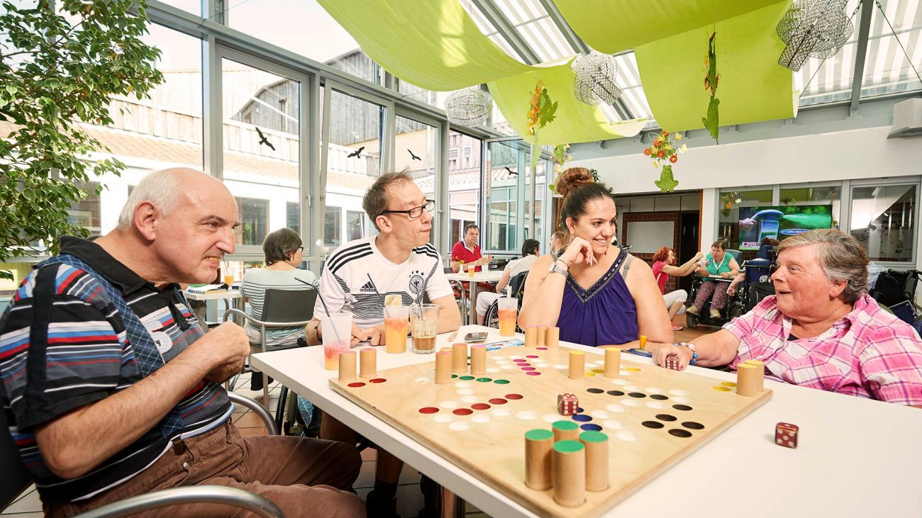 Gemeinsamer Spieletag in der Cafeteria: Mehrere Personen sitzen um einen Tisch und spielen Mensch ärger dich nicht