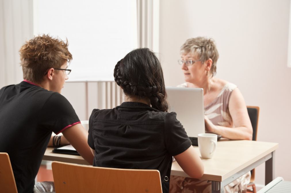 Zwei Menschen sitzen am Tisch und werden von einer professionell Berater*in unterstützt