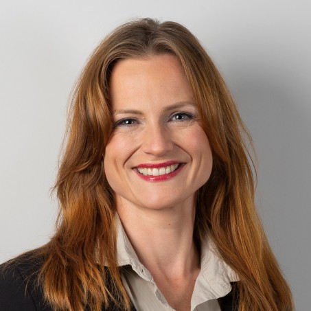 Eine Frau mit braun/rötlichen Haaren lächelt mich sichtbaren Zähnen in die Kamera.