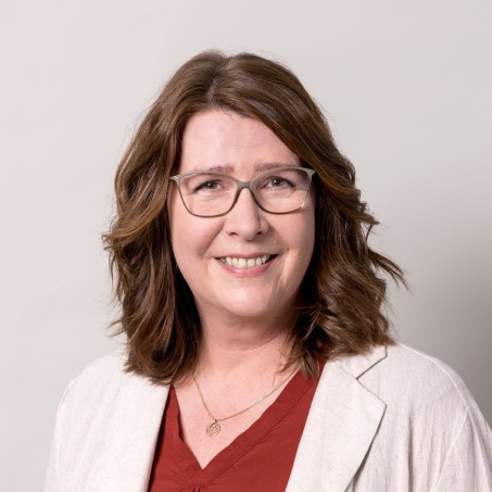 Eine Frau mit dunklen schulterlangen Haaren und einer rundlichen Brille lächelt mich sichtbaren Zähnen in die Kamera.