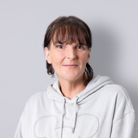 Eine Frau mit dunklen Haaren und Pony schaut freundlich in die Kamera.